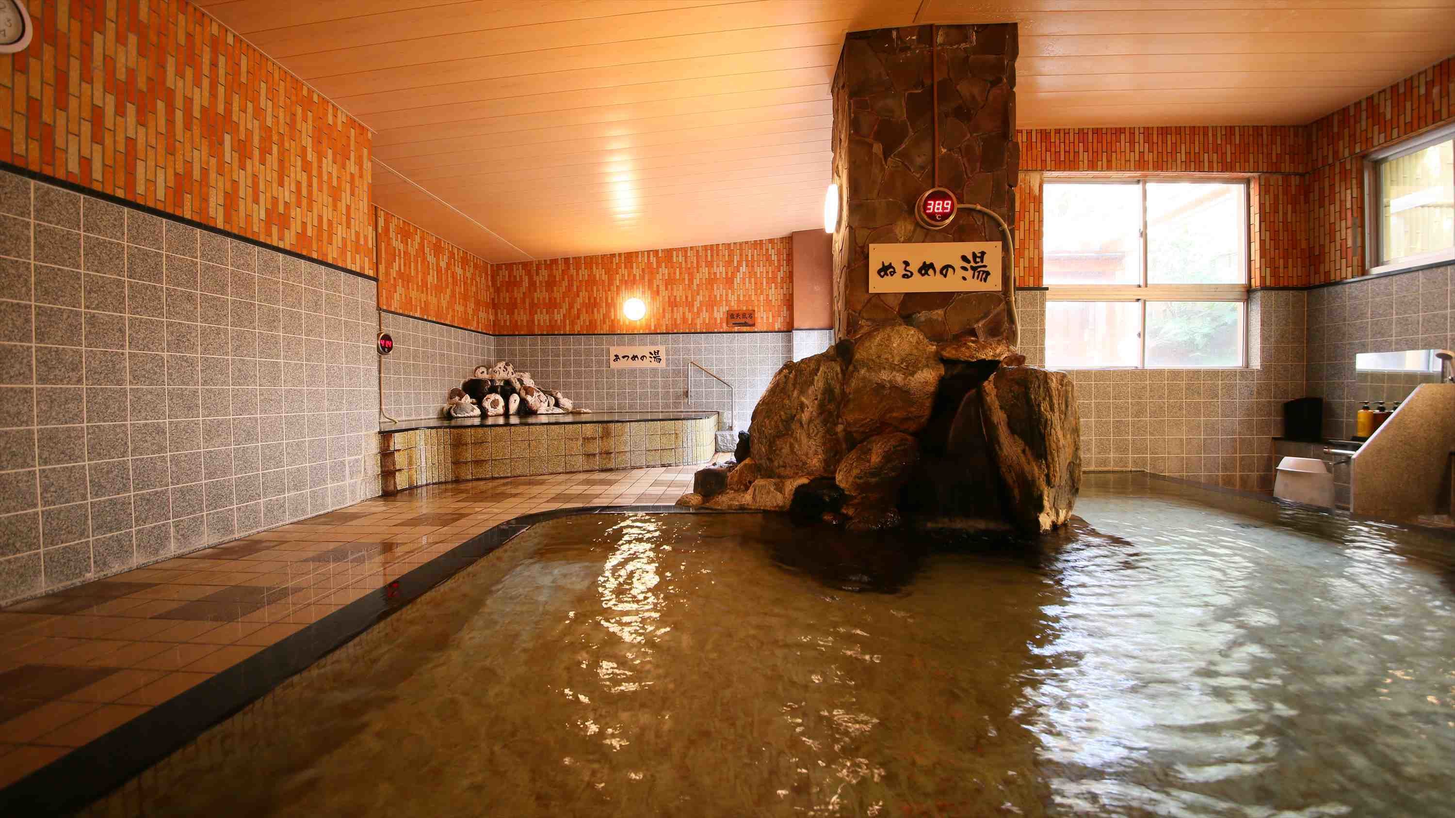 Un onsen japonés tradicional con una bañera de roca, paredes de azulejos y techo de madera.