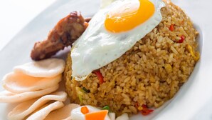 A plate of fried rice topped with a fried egg, accompanied by a piece of fried chicken, a slice of cucumber, and a small portion of pickled vegetables. - Amaris Hotel Malioboro Yogjakarta (Yogyakarta)