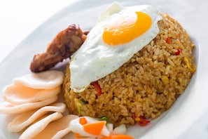 A plate of fried rice topped with a fried egg, accompanied by a piece of fried chicken, a slice of cucumber, and a small portion of pickled vegetables.