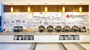 Un buffet disposé devant une fresque représentant un paysage urbain, avec un logo et divers récipients contenant de la nourriture.