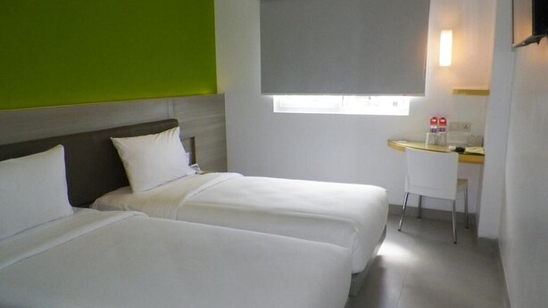 Une chambre d’hôtel avec deux lits, un petit bureau, une fenêtre avec un store et un mur d’accent vert.