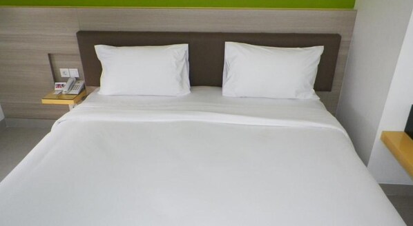 Una habitación de hotel con una cama, dos almohadas, una mesita de noche con un teléfono y una pared verde.