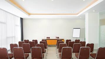 A conference room with rows of chairs facing a podium, a whiteboard, and a glass partition.