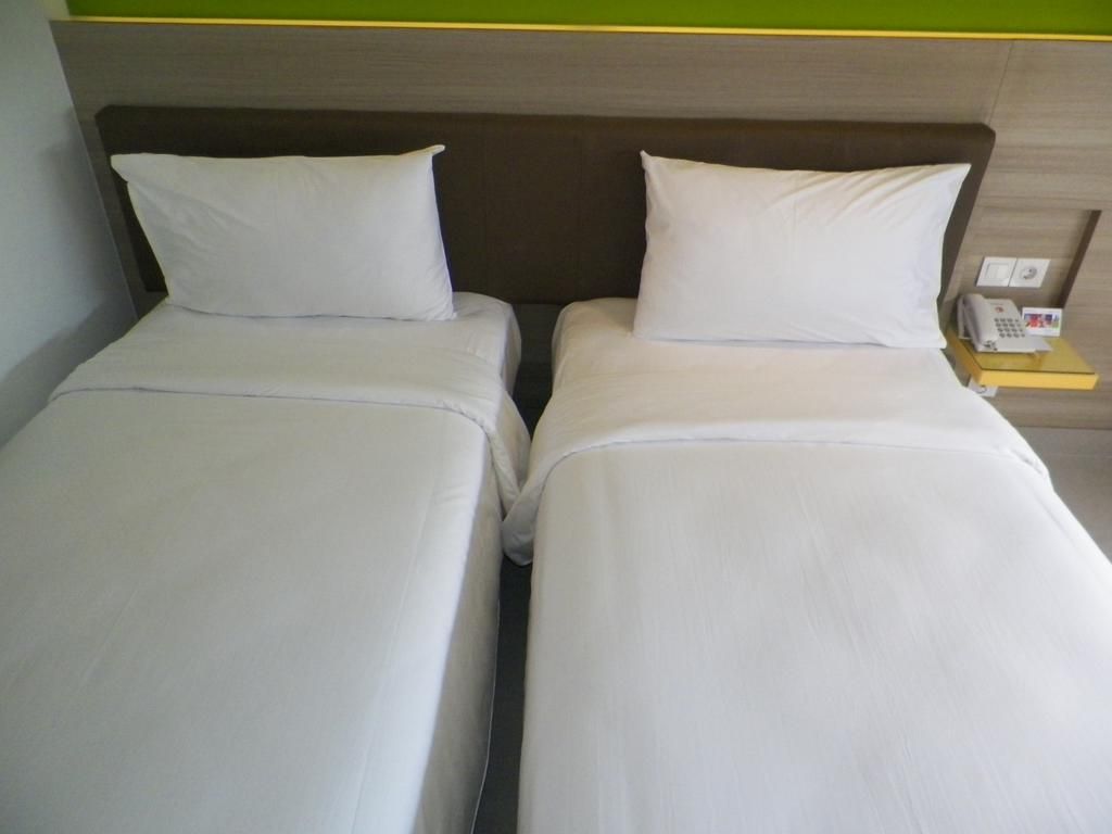 Two single beds with white linens, a wooden headboard, and a bedside table with a telephone.