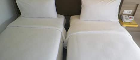 Two single beds with white linens, a wooden headboard, and a bedside table with a telephone.