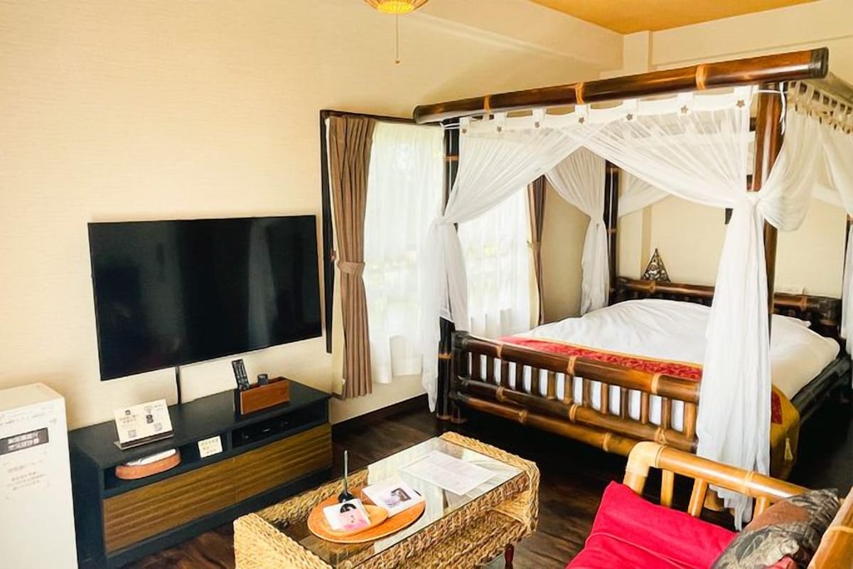 A room with a bed, a television, a desk, and a wicker basket.