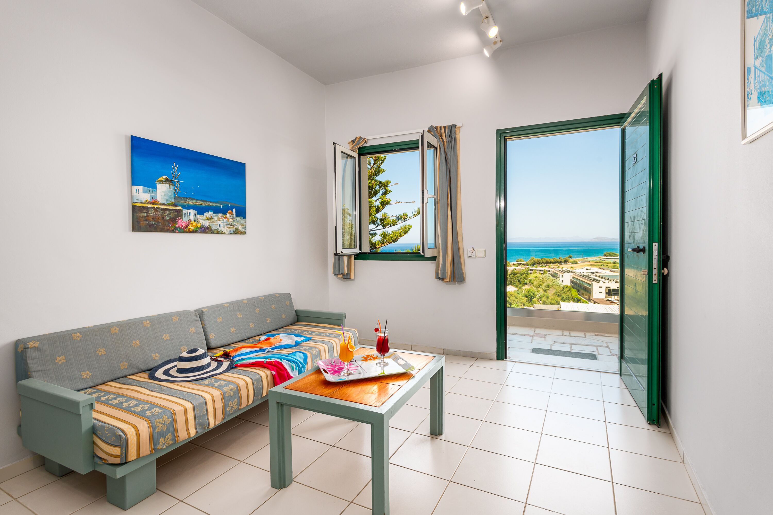 A modern living room with a sofa, a coffee table, a painting, and a view of the sea through a window.