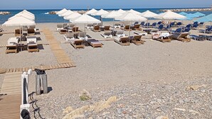Una playa con filas de tumbonas y sombrillas, un paseo de madera y un litoral rocoso.