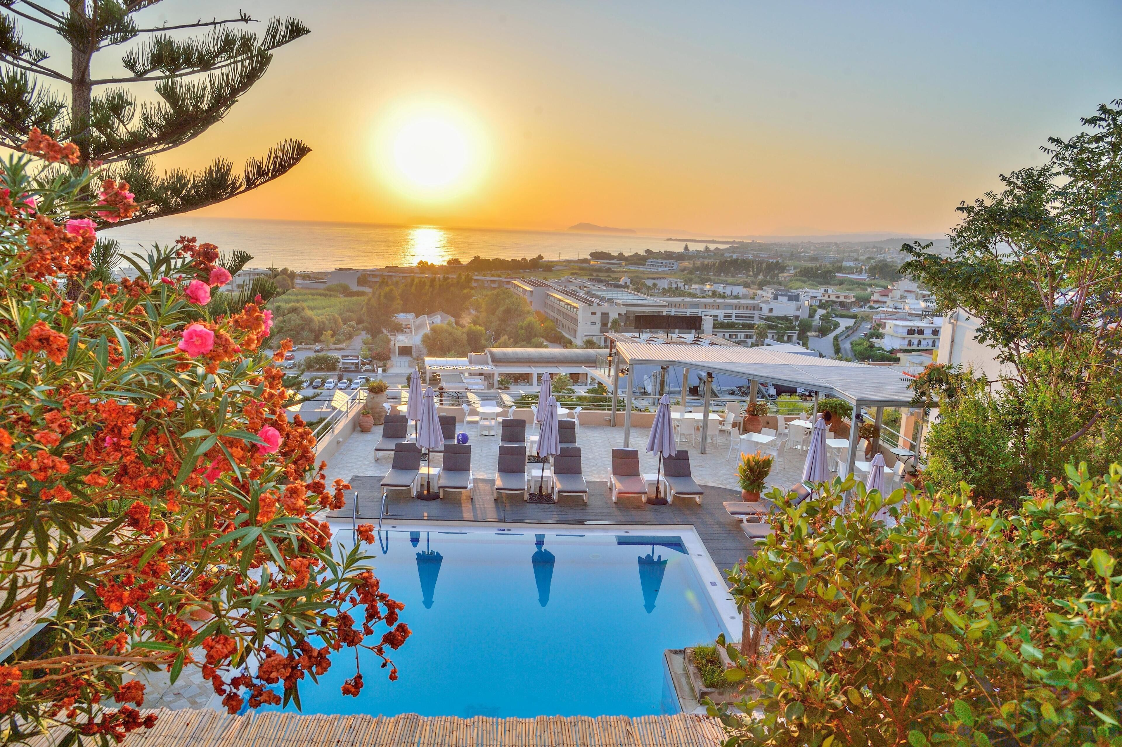 A poolside area with lounge chairs and umbrellas, overlooking a body of water and buildings in the distance.