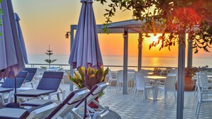 Una terraza con tumbonas y sombrillas, con vista al mar al atardecer.