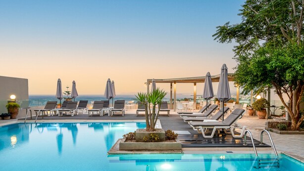Zona de piscina con sillones y sombrillas, una pequeña isla con plantas y vista al mar.