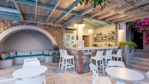 Una zona de bar con sillas y mesas blancas, una pared de piedra y un banco de asientos.
