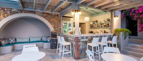 A bar area with white chairs and tables, a stone wall, and a seating bench.