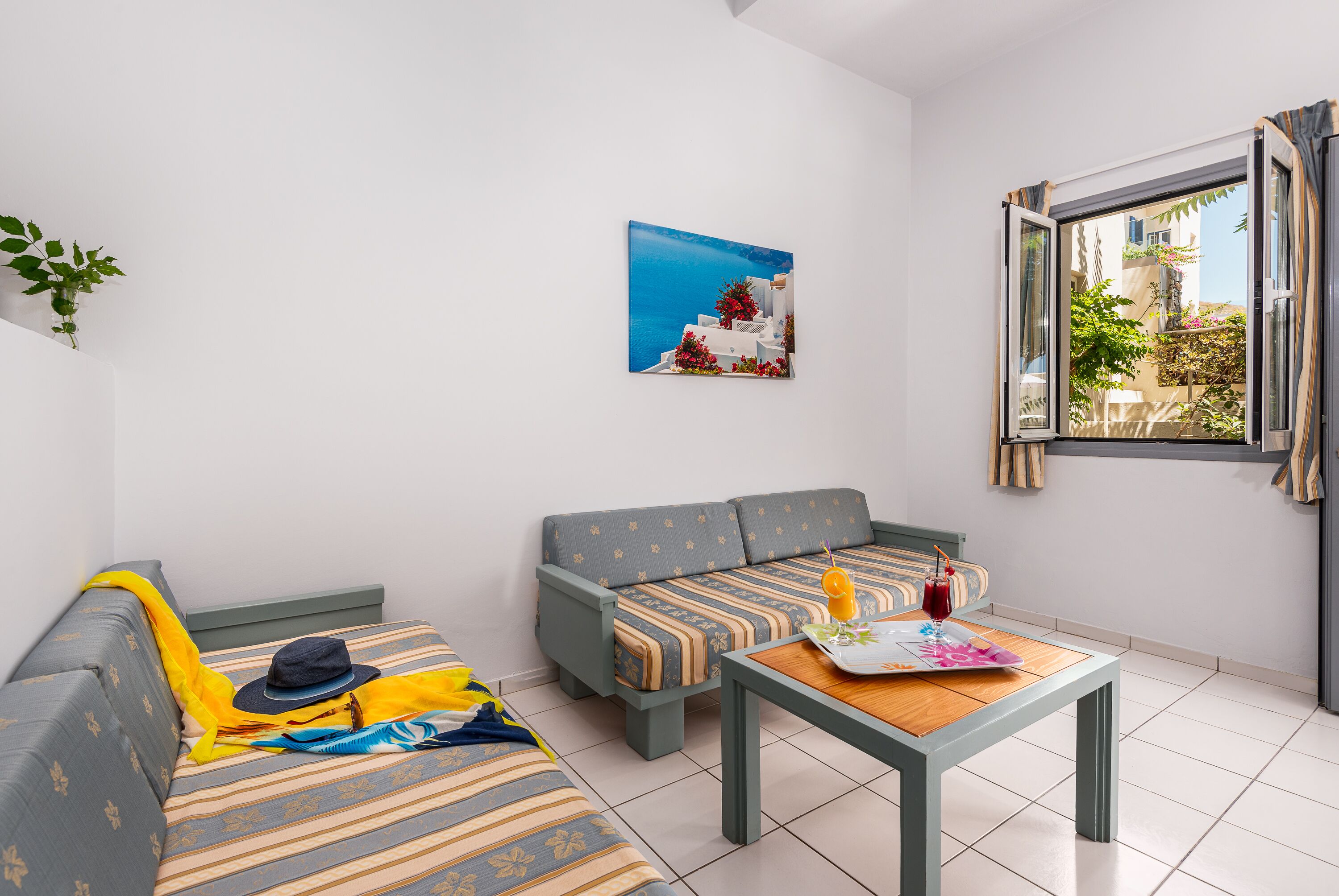 A modern living room with a sofa, a small table, and a window with a view of a building and greenery.