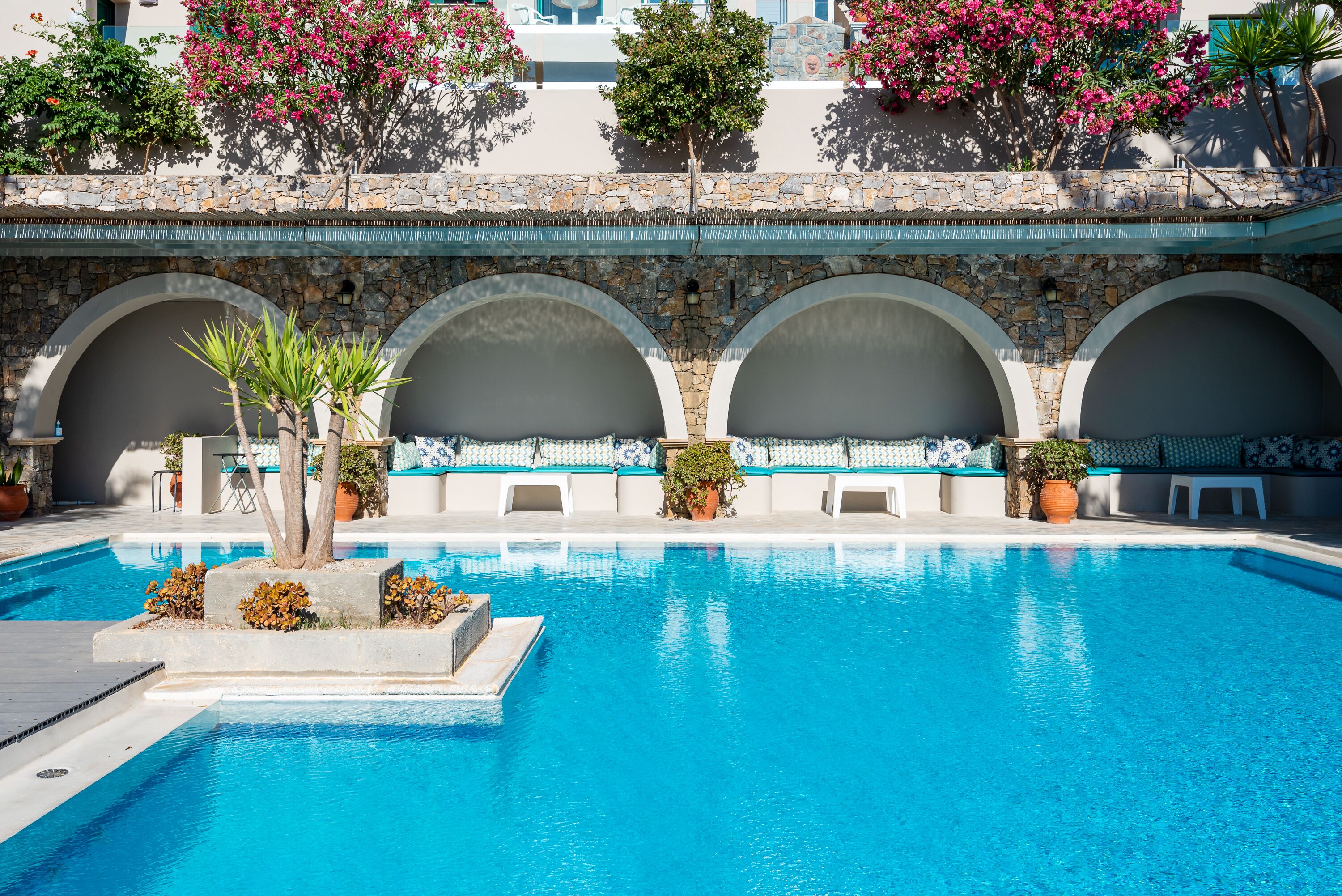 A swimming pool with clear blue water, surrounded by stone arches and potted plants.