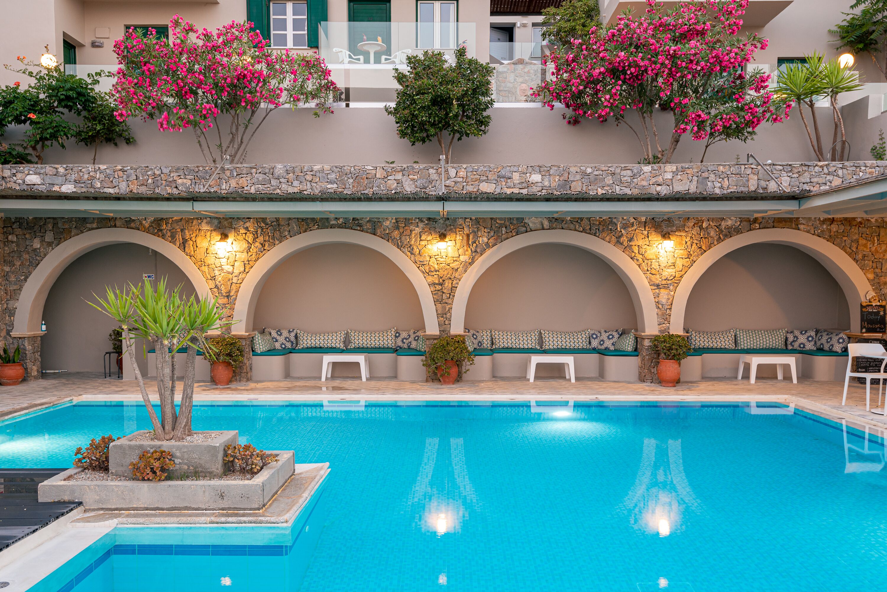 Una piscina con pared de piedra, zonas de estar y plantas en macetas.