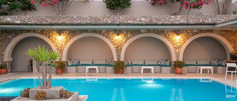 A swimming pool with a stone wall, seating areas, and potted plants.