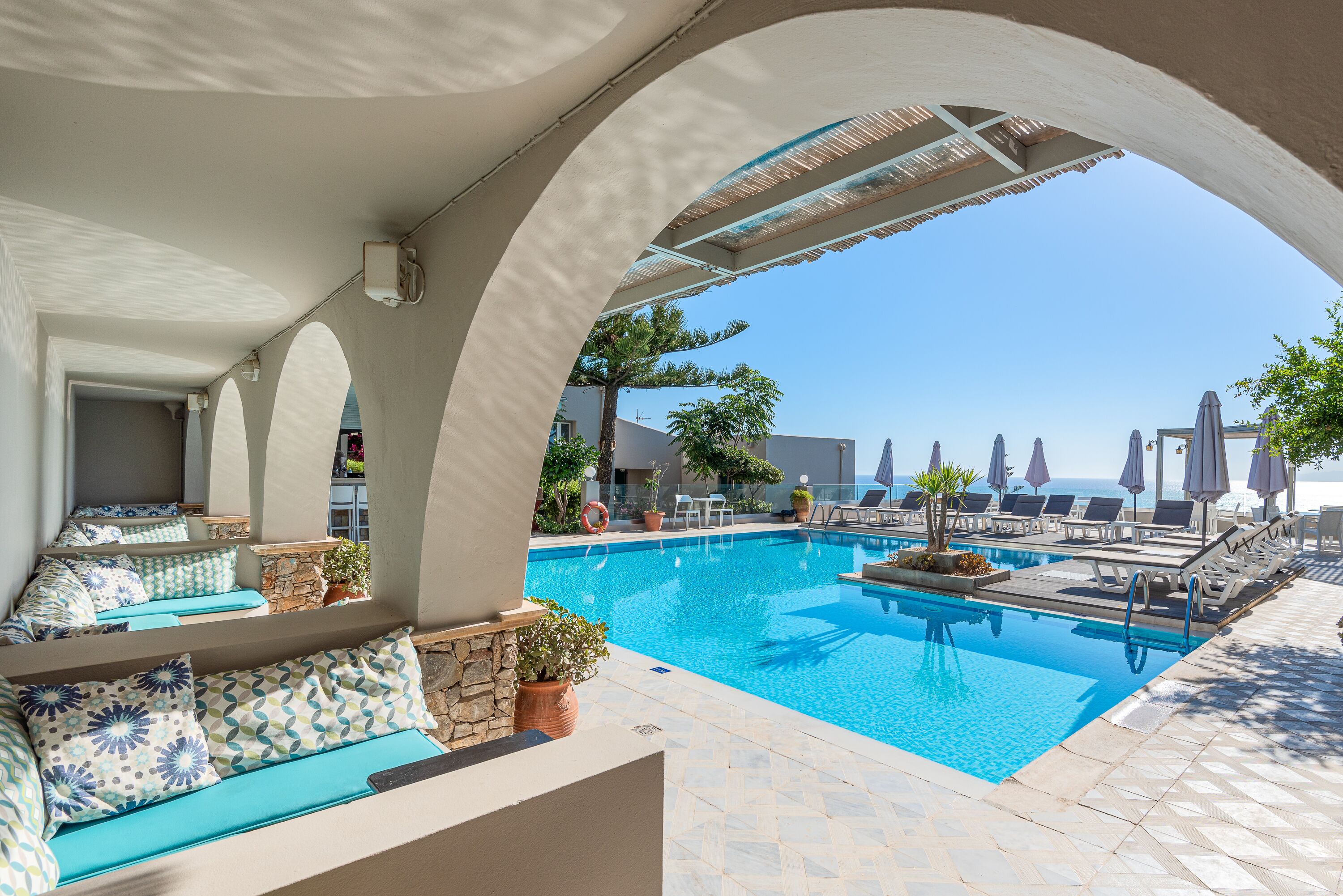 A poolside area with lounge chairs, a seating area with cushions, and a view of the sea.