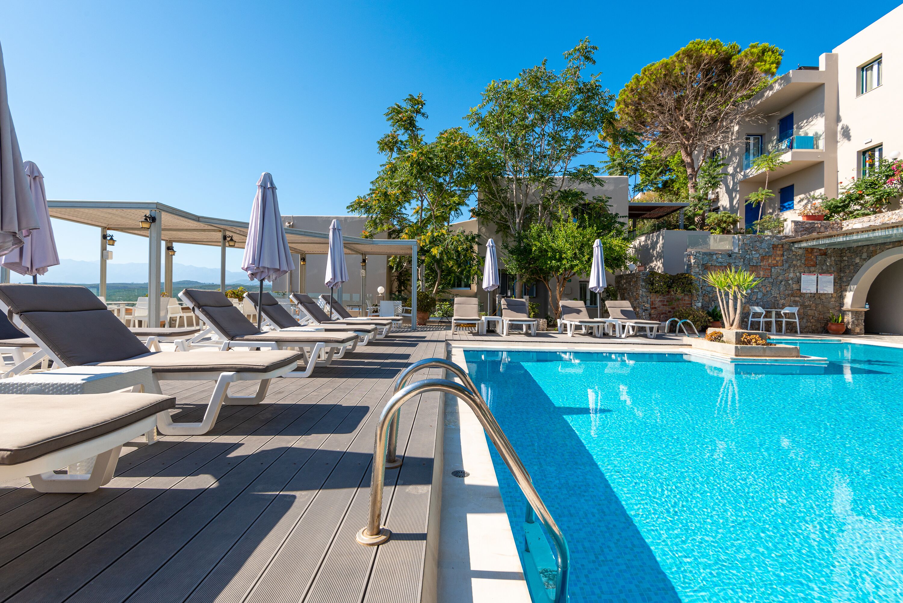 A poolside area with lounge chairs and umbrellas, a clear blue pool, and a view of the sea.