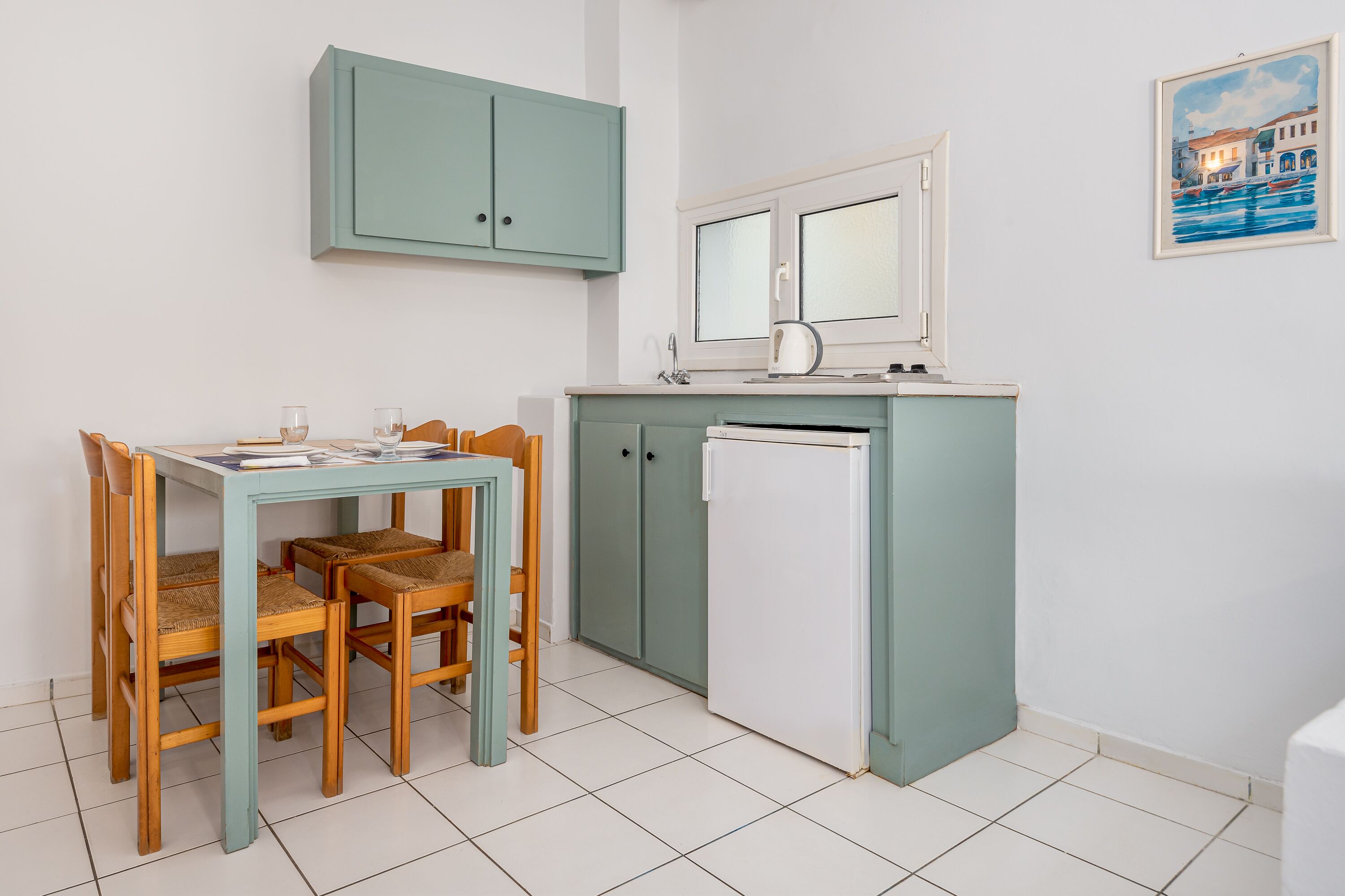 Une cuisine compacte comprenant une table et des chaises, un réfrigérateur et une fenêtre donnant sur des immeubles.
