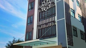 A modern building with a large flower logo, multiple floors, and a covered entrance area. - Serene Residence (Kanchanaburi)