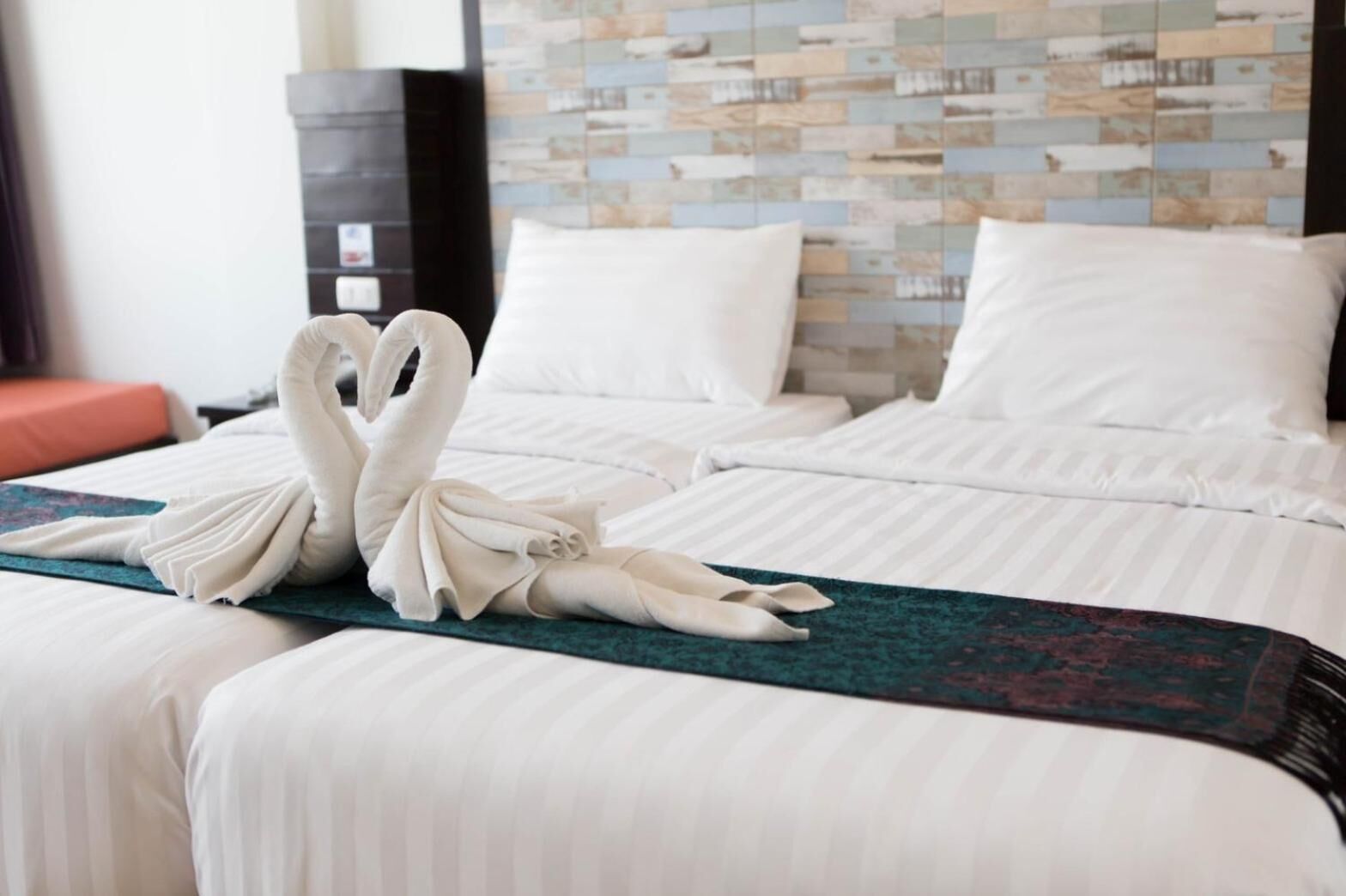 A hotel room with two beds, a teal accent rug, and a wall with a mosaic pattern.