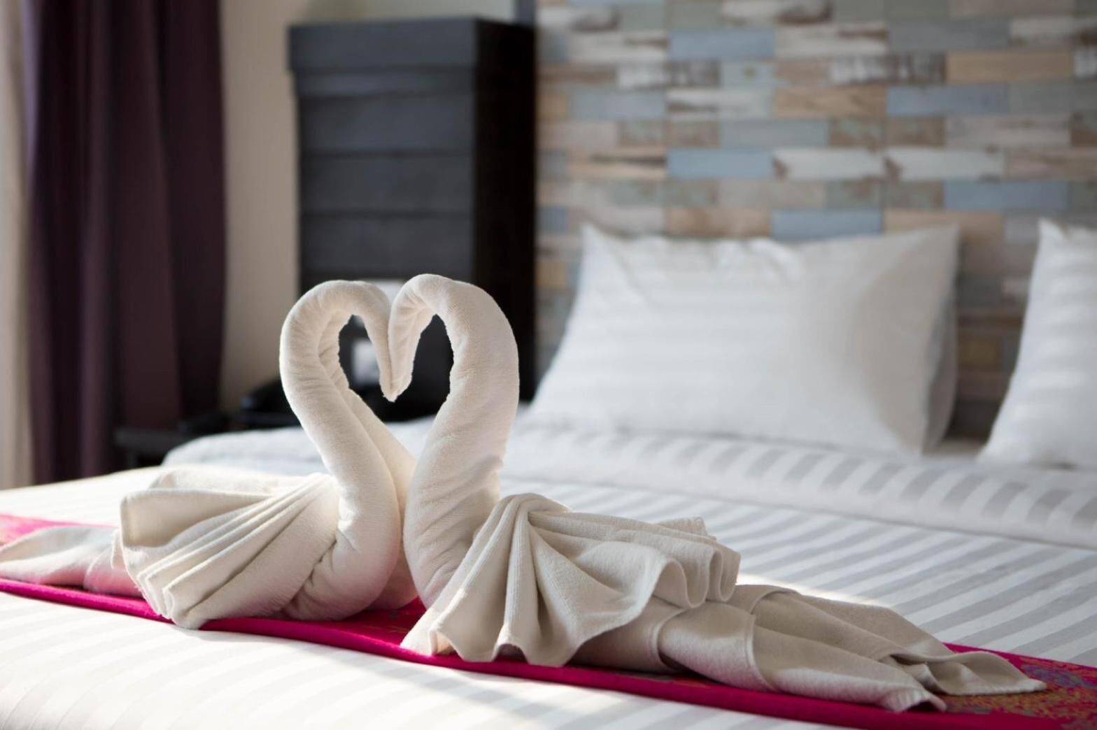 Ein Bett mit einer herzförmigen Handtuch-Anordnung und einer rosa Bettdecke.
