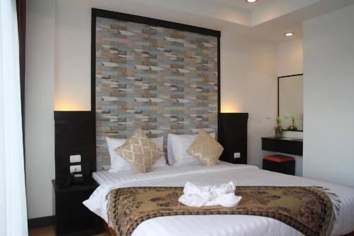 Hotellihuone, jossa on sänky, yöpöytä, lipasto ja kuviollinen seinä.
