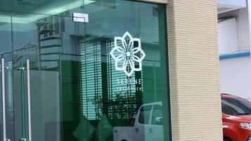 Un edificio con fachada de vidrio, un logotipo con el texto "SERENE residence", y el reflejo de un coche y un edificio en el cristal.