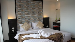 A hotel room with a large bed, two nightstands, a wall with a patterned design, a mirror, and a small table with a vase of flowers. - Serene Residence (Kanchanaburi)