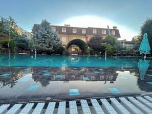 A swimming pool with a clear reflection, surrounded by greenery and a building with a large archway. - Sharq Hotel (Tashkent)