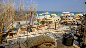 Een terras aan het strand met buitenmeubilair, parasols en uitzicht op de oceaan.