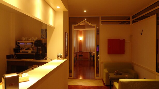 Quarto de hotel com cozinha compacta, área de estar com sofá e poltronas, parede com destaque em vermelho e vista para a sala de jantar.