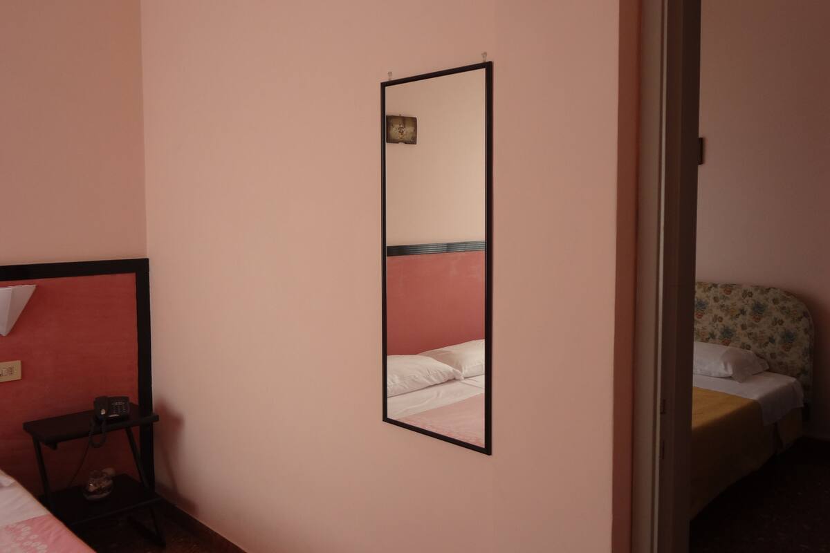 A room with a bed, a bedside table with a lamp, and a mirror on the wall.