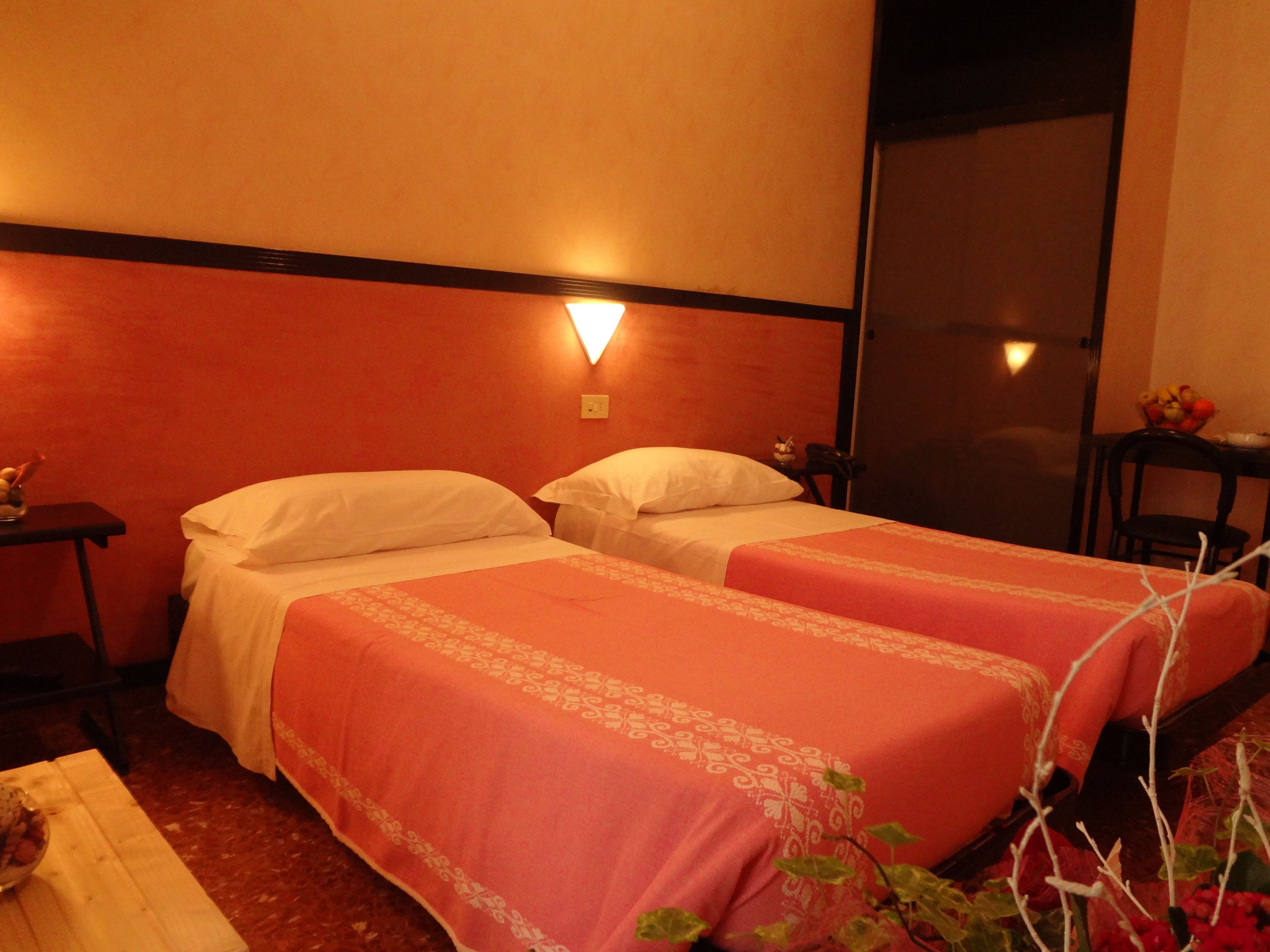 Una camera d'albergo con due letti, un comodino, una lampada a parete e una porta.