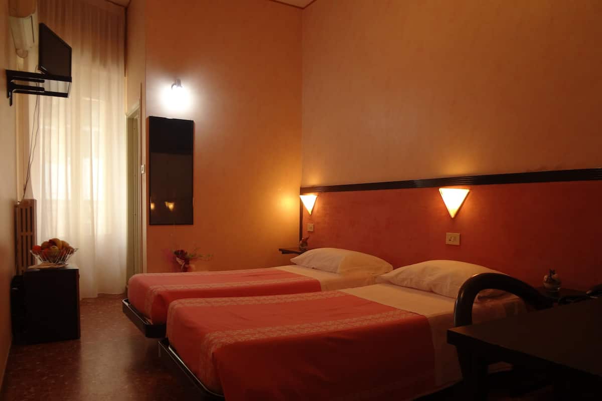 A hotel room with two beds, a desk, a chair, a nightstand, a lamp, and a mirror.