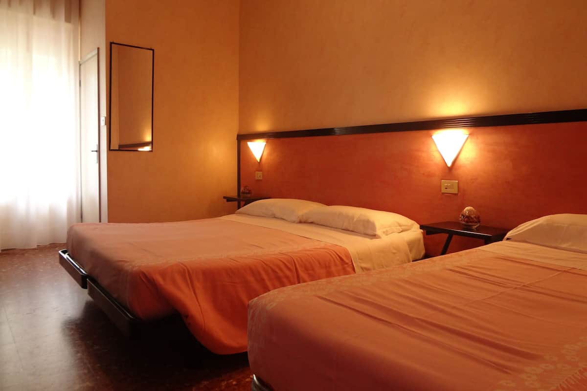 A hotel room with two beds, each with a wooden headboard and a nightstand. There is a mirror on the wall and a small table with a decorative item.