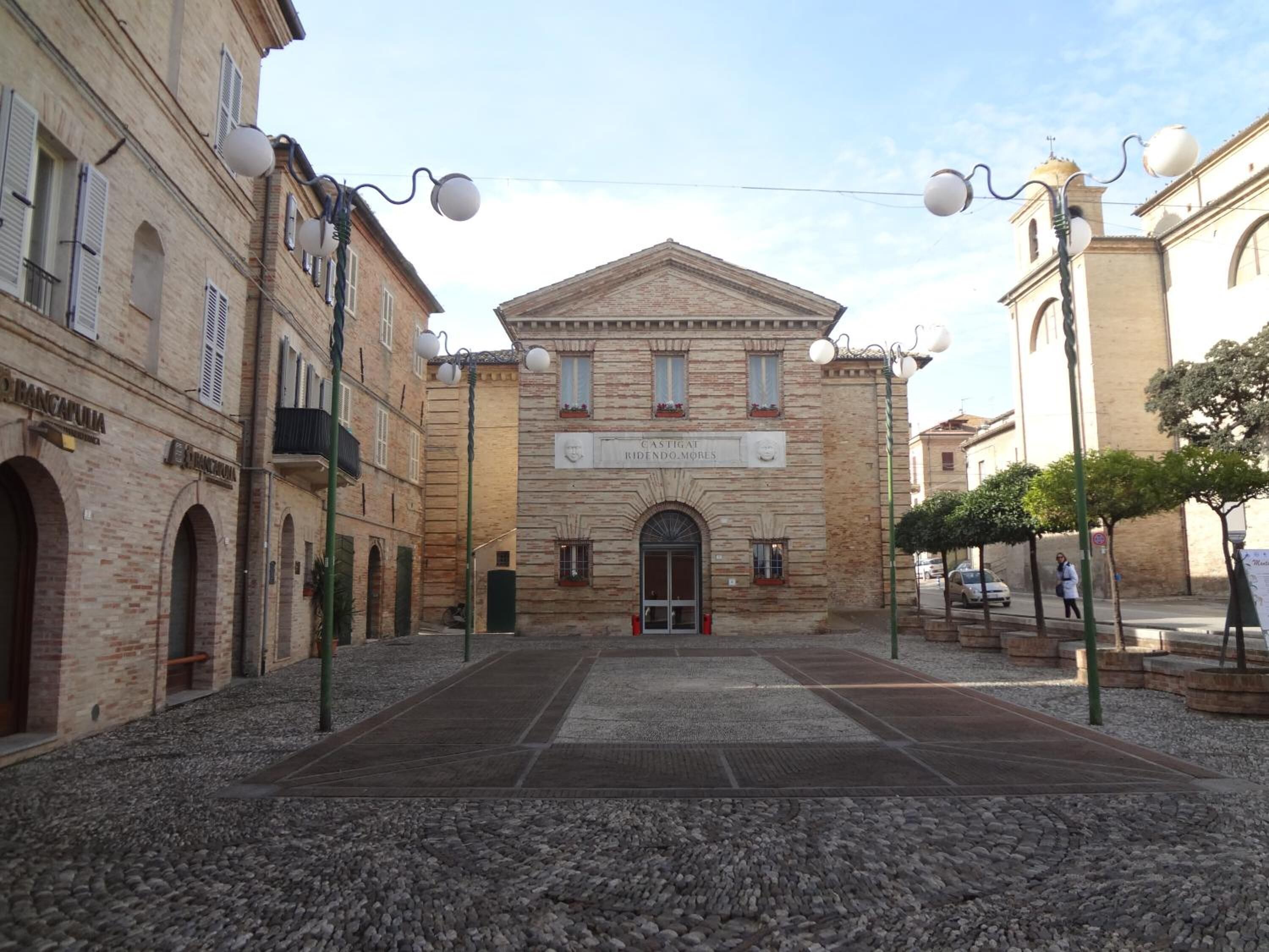 Un edificio storico con un ingresso centrale, affiancato da elementi architettonici tradizionali e un cortile in pietra.