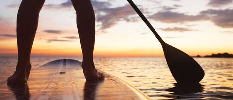 A person standing on a surfboard at the beach during sunset.