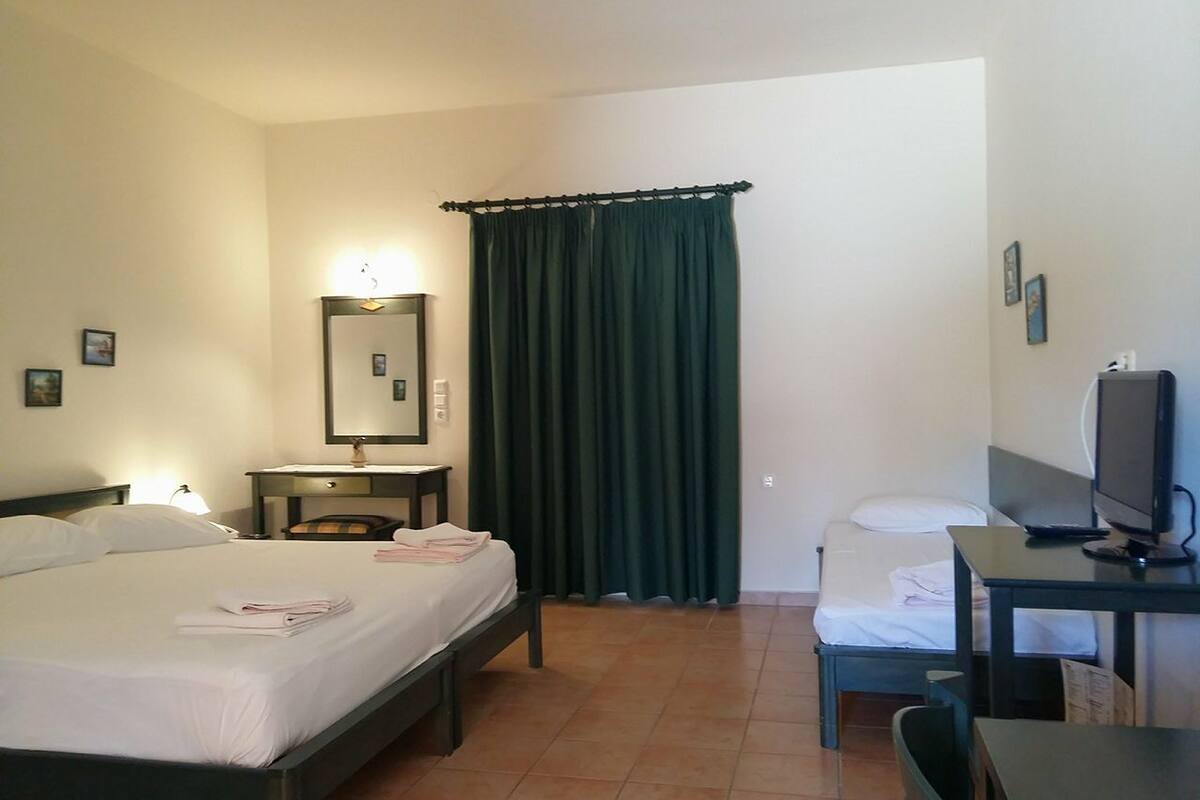 A hotel room with two beds, a desk, a chair, a television, and a window with curtains.