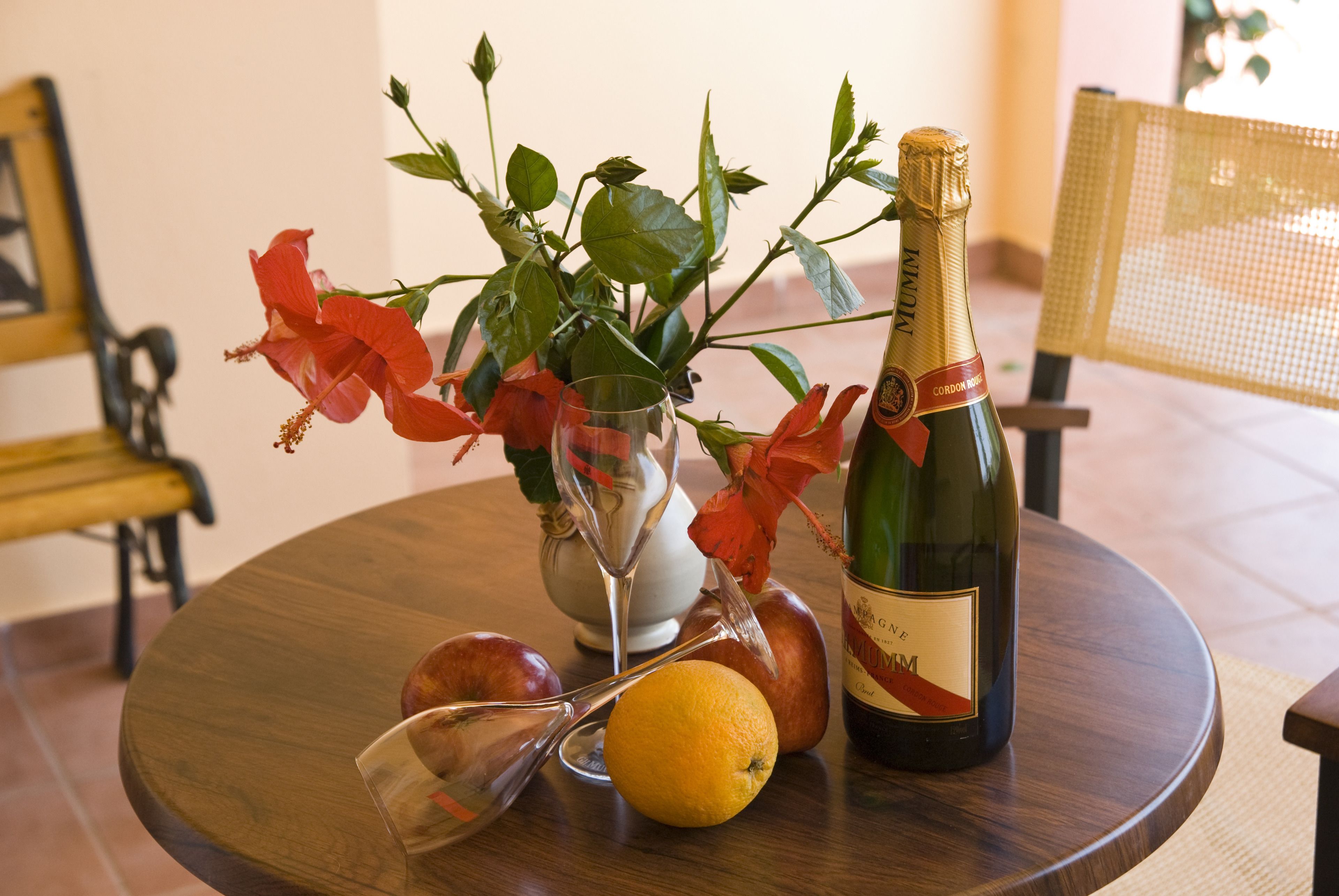 A table with a bottle of champagne, a glass, an orange, and a vase with flowers.