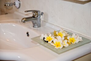 A bathroom sink with a chrome faucet and a glass tray holding white and yellow flowers. - Kallicrates Village (Sfakia)