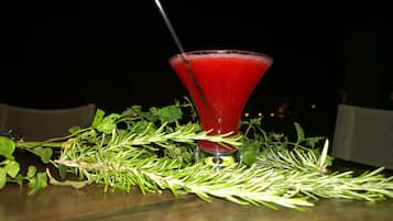 Un vaso de cóctel con una bebida roja sobre una mesa rodeada de ramitas de romero.