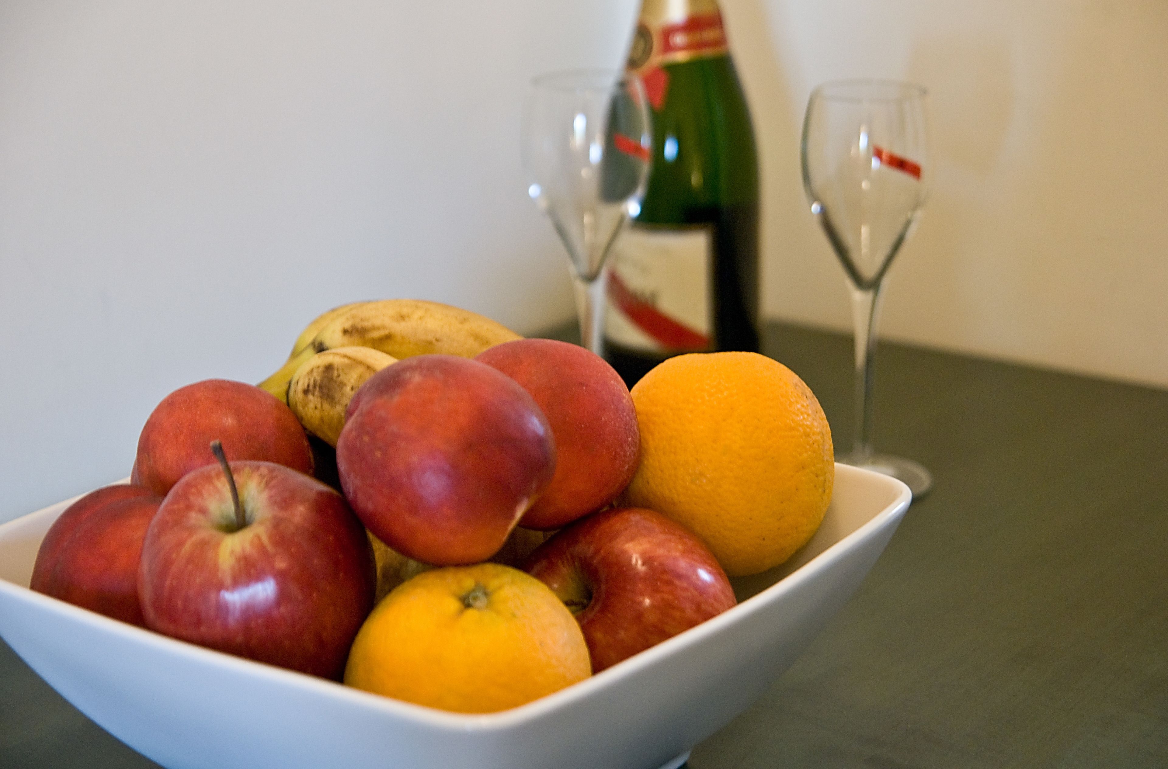 A bowl of fruit with apples and oranges on a table.