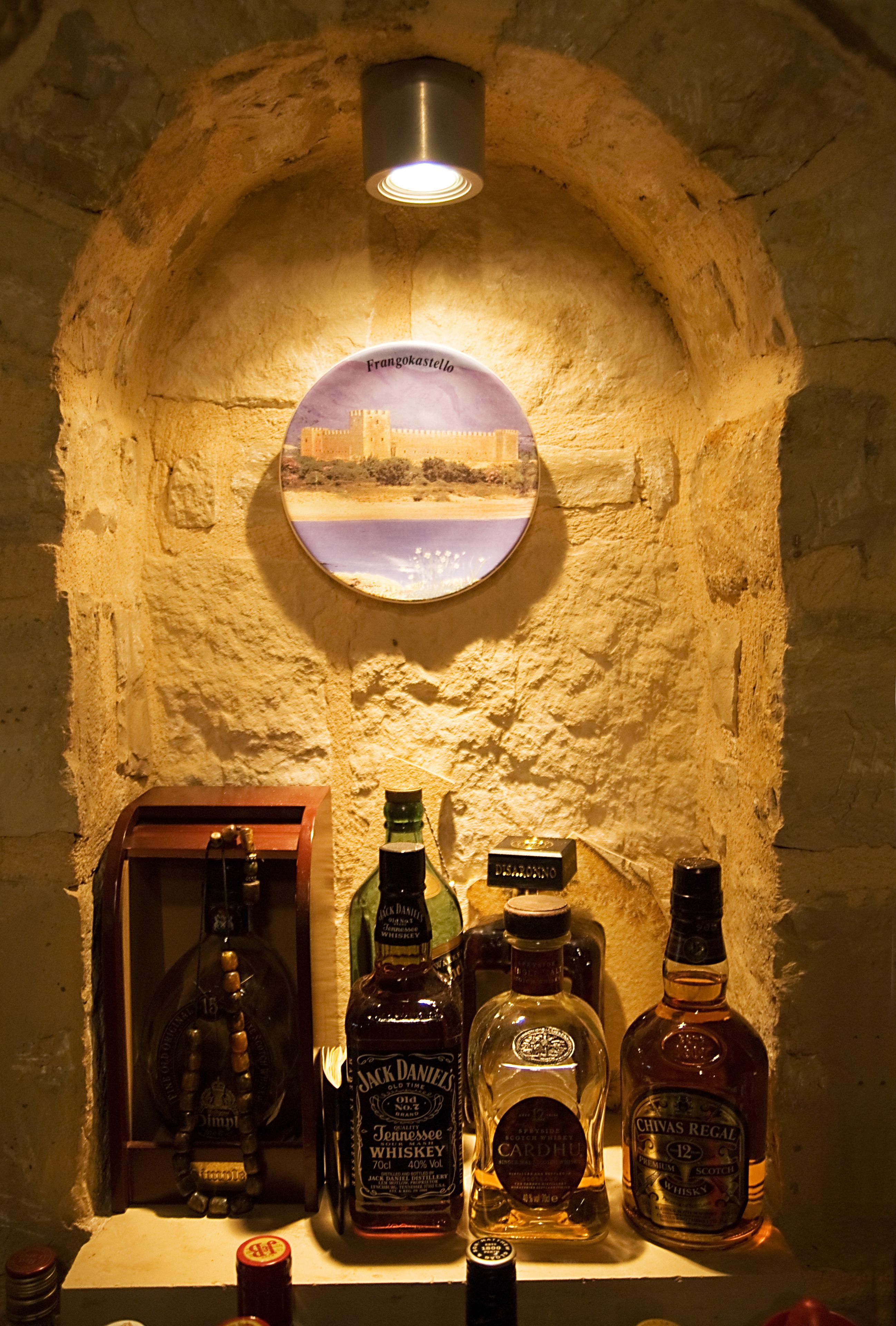 Una colección de botellas de whisky en un nicho de piedra con un cuadro enmarcado de un paisaje urbano.