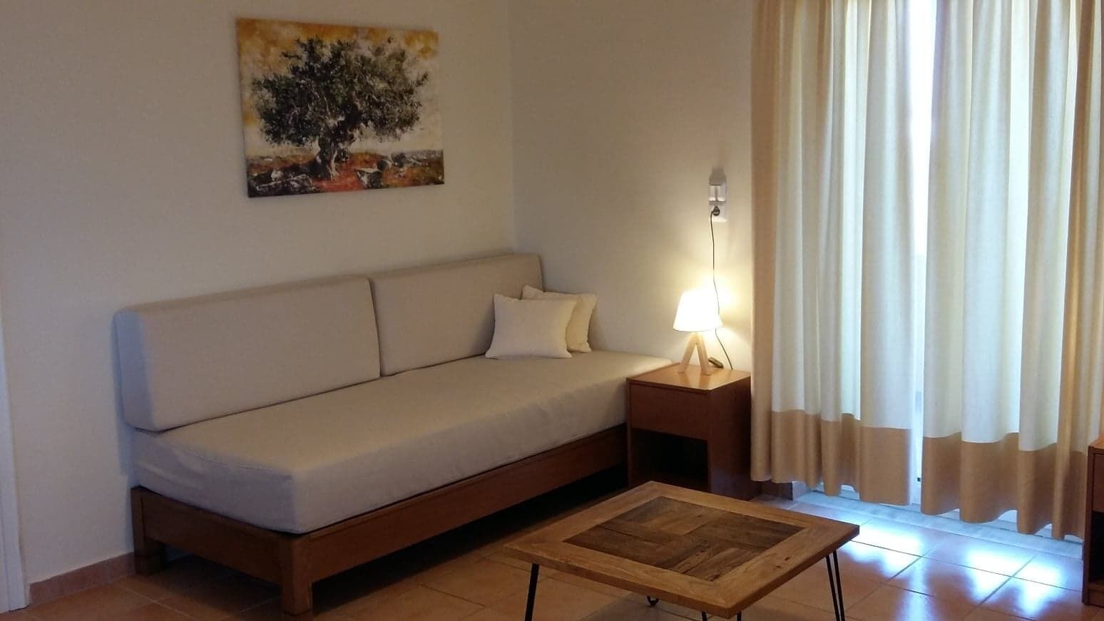 A living room with a sofa, a wooden coffee table, a lamp, and a painting on the wall.
