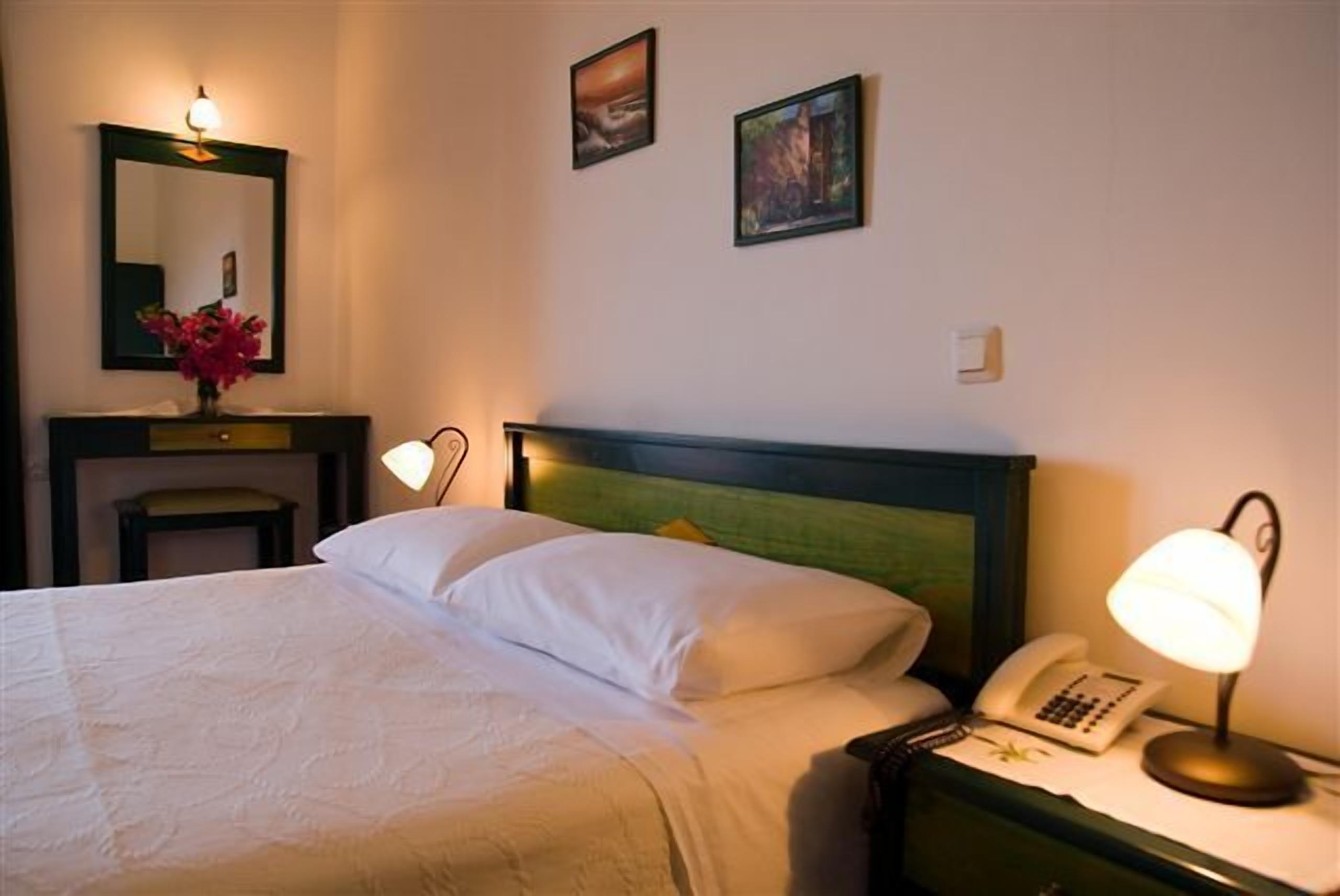 Un letto rifatto con lenzuola bianche, una lampada da comodino, un telefono e un piccolo tavolo con un vaso di fiori.