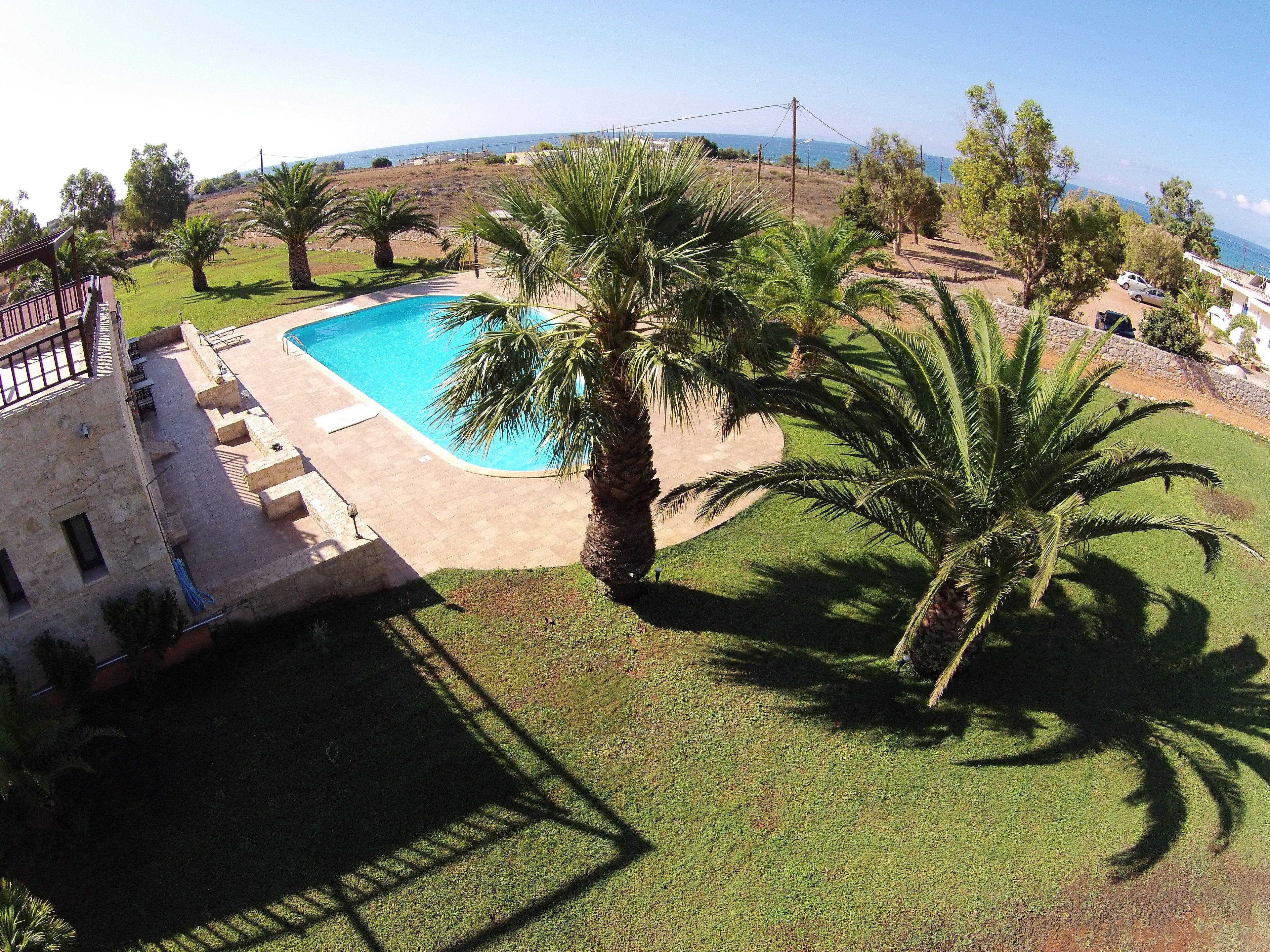 Ein Pool mit einer Steindeck, umgeben von Palmen und Blick auf das Meer.