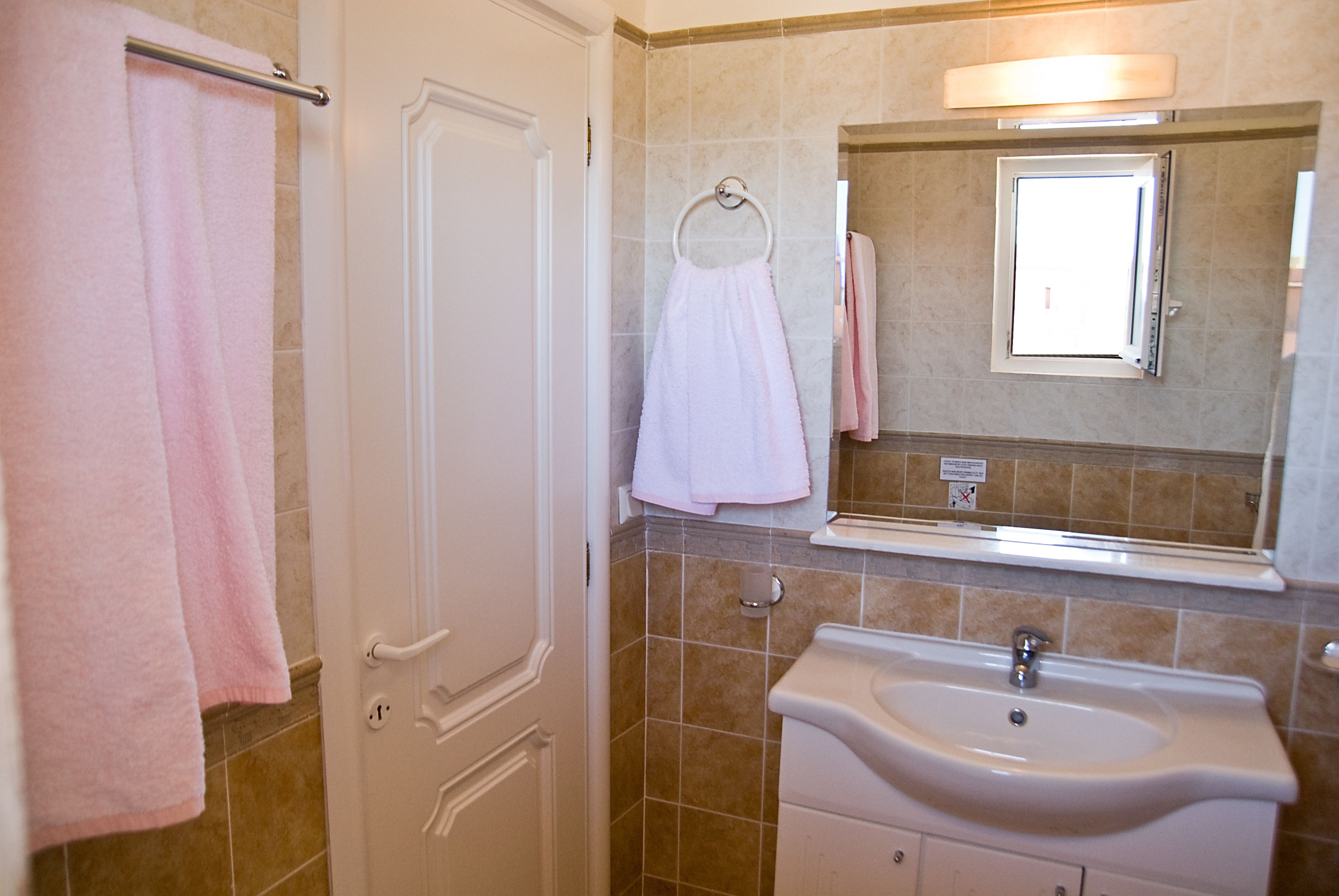 A bathroom with a white sink, a mirror, and beige tiles.