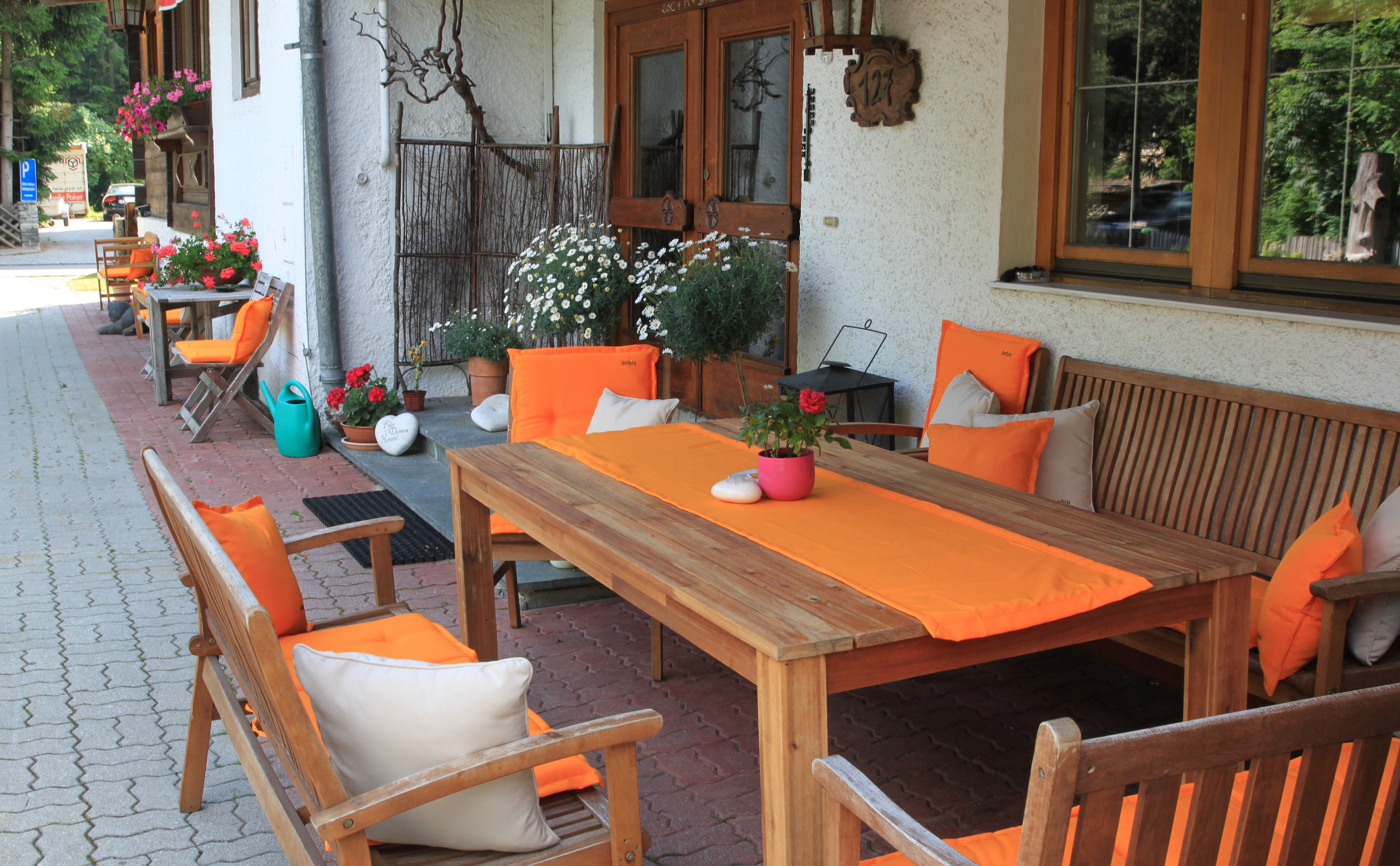 Una terrazza esterna con tavolo e sedie di legno, circondata da vasi con piante e fiori.